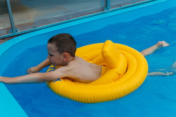 Αγόρι Κολυμπάει Στο Νερό Ένα Φουσκωτό Κίτρινο Κύκλο Στην Πισίνα — Φωτογραφία Αρχείου