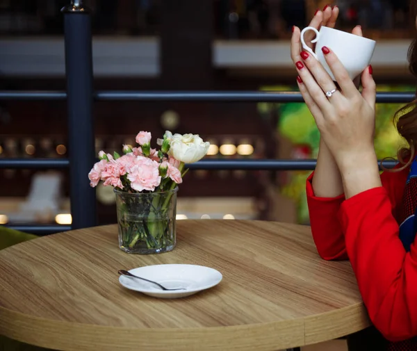 Дівчина з чашкою кави за столом у червоній шубці на дерев'яному фоні столу — стокове фото