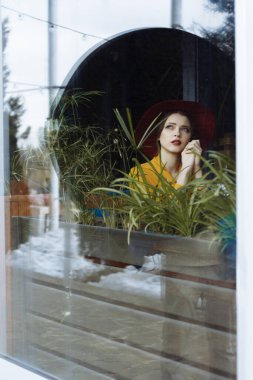 Elbiseli ve şapkalı kız pencereden dışarı bakıyor, üzgün, kendini izole, depresyon, salgın