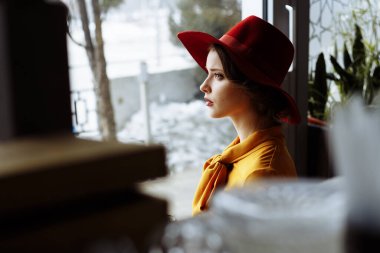 Elbiseli ve şapkalı kız pencereden dışarı bakıyor, üzgün, kendini izole, depresyon, salgın