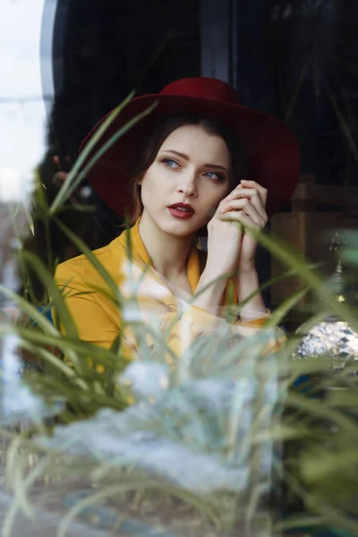 Chica en un vestido y un sombrero mira por la ventana, triste, auto-aislamiento, depresión, pandemia — Foto de Stock