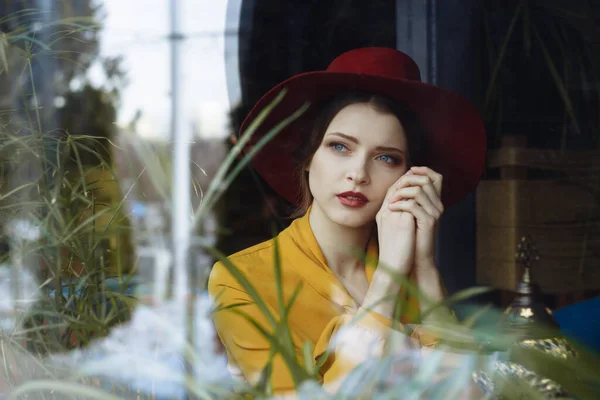 Chica en un vestido y un sombrero mira por la ventana, triste, auto-aislamiento, depresión, pandemia — Foto de Stock