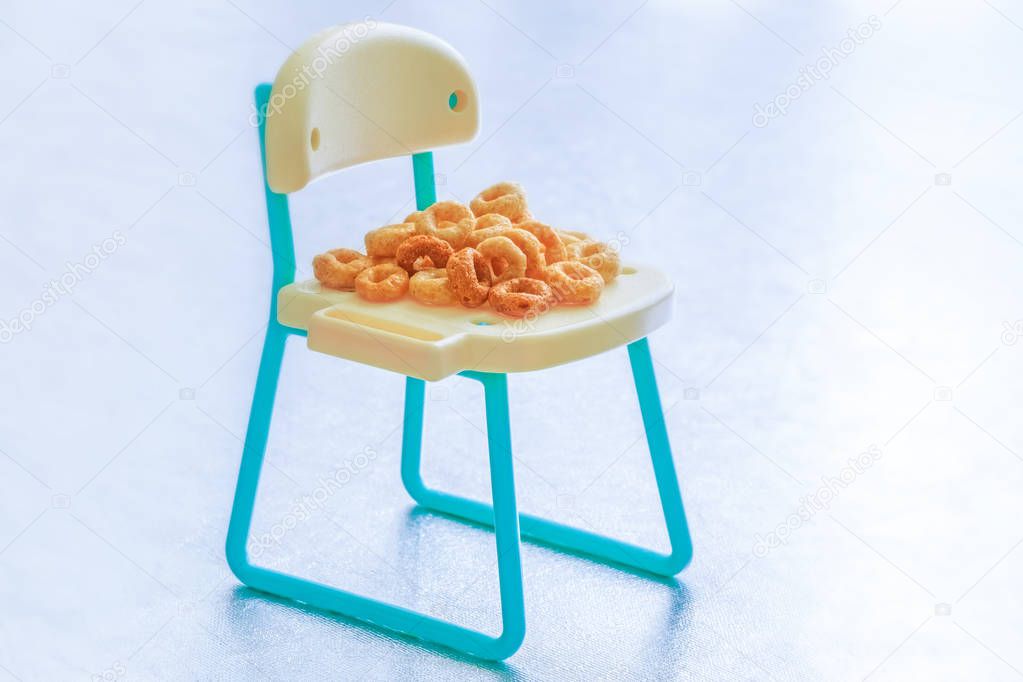 Pile of a lot of round breakfast cereals isolated on miniature chair. Healthy cereal rings on seat. Conceptual picture for cereals, kids food & healthy breakfast. 