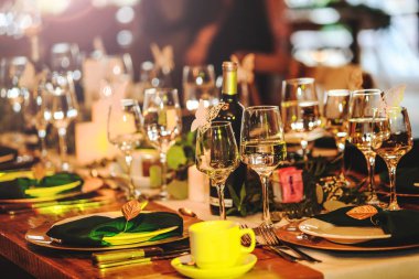 Some wine glasses, plates, forks and green briefcases for event celebration. Beautiful dinner table setting. Vintage decoration of reception table. Elegant arrangement of the holiday tableware. Banquet or holiday background in a rustic atmosphere.