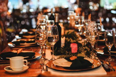 Beautiful dinner table setting. Vintage decoration of reception table. Elegant arrangement of the holiday tableware. Wine glasses, plates, forks and green briefcases for event celebration. Banquet or holiday background in a rustic atmosphere.  