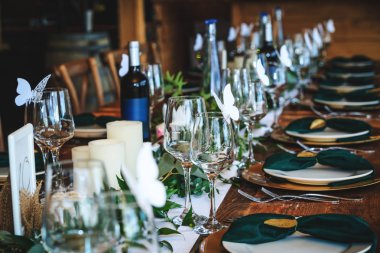 Wine glasses, plates, forks and green briefcases for the banquet. Rustic wedding table setting in fancy Canadian restaurant. Vintage decoration of reception table. Elegant arrangement of the holiday tableware. 