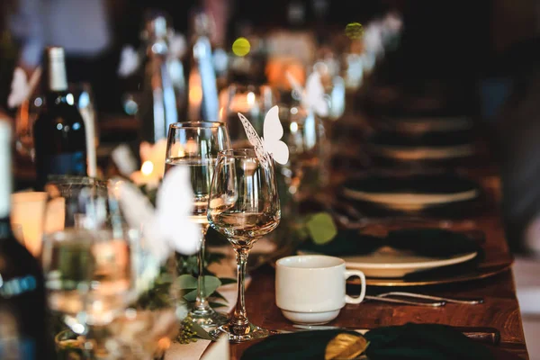 Banquet or holiday background in a rustic atmosphere.  Dinner table setting. Vintage decoration of reception table. Elegant arrangement of the holiday tableware. Wine glasses, plates, forks and green briefcases for event celebration.