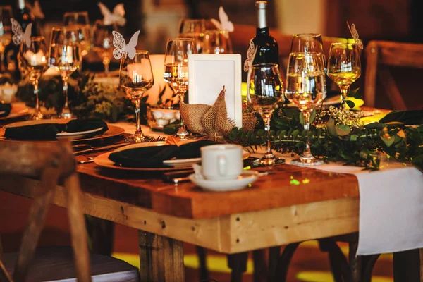 Elegant arrangement of the holiday tableware. Vintage decoration of reception dinner table. Rustic wedding table setting in fancy American restaurant. Wine glasses, plates, forks and green briefcases for the banquet.