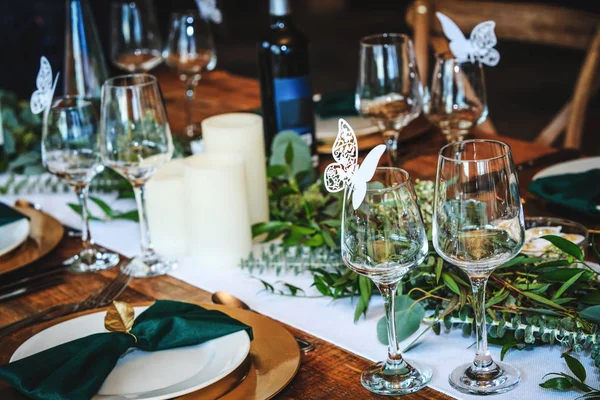 Rustieke trouwtafel in een chique Amerikaans restaurant. Vintage decoratie van de receptie tafel. Elegante inrichting van het servies. Wijnglazen, borden, vorken en groene aktetassen voor het banket — Stockfoto