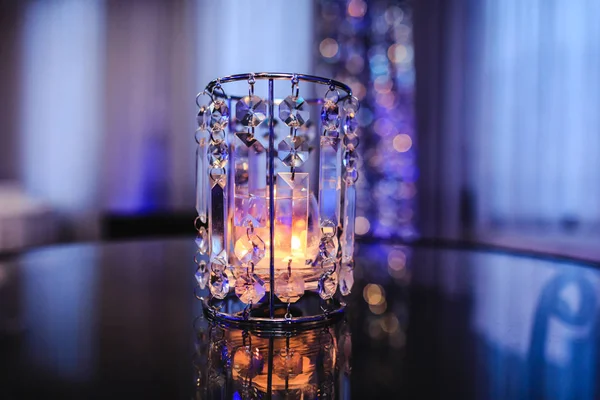 Crystal glass light indoor of party hall. Glass candle light on background of the purple events room. Beautiful violet decoration in modern banquet restaurant. Holiday table setting. Romantic background for event celebration.