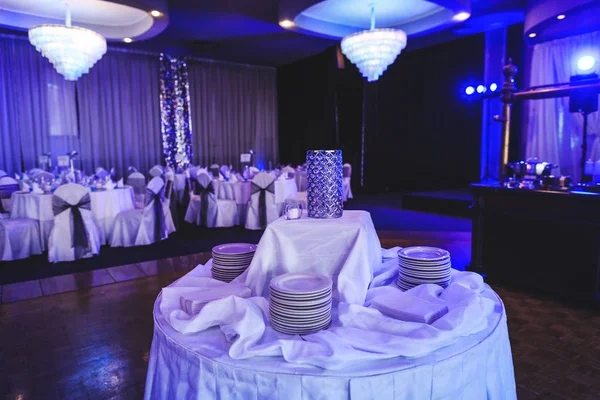 Banquet hall before party. Tableware and tablecloth arrangement in interior of modern ceremony room. Luxury place for wedding, anniversary and other events. Elegant decor with chandelier and table setting indoor of restaurant.