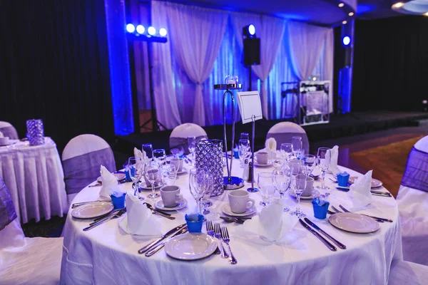 Tafelgerei en tafelkleed arrangement in het interieur van de moderne ceremonie kamer. Banketzaal voor het feest. Luxe plek voor bruiloft, jubileum en andere evenementen. Elegante inrichting met kroonluchter en tafel setting binnen in restaurant. — Stockfoto