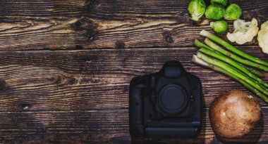 Kamera ve sebzeler ahşap arka planda, yemek fotoğrafçılığı konsepti olarak. Profesyonel yemek fotoğrafçıları, sosyal medya veya blog yazarları için yaratıcı kavramsal resim. Mutfak bahçesiyle kompozisyonda fotoğraf ekipmanları.