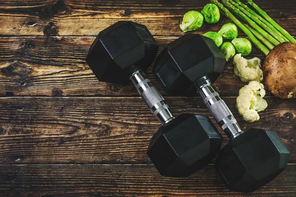Dambıllar ve taze sebzeler ahşap arka planda. Spor ya da sağlık yaşam tarzı kavramsal resim. Aktif spor ve sağlıklı beslenme konsepti. Atletizm olimpiyatları için diyet planı ve... Fitness pankartları ve diğer arkaplanlar için en iyisi.
