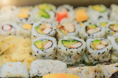 Suşi, somon, avokado, ton balığı ve salatalıklı olursa harika olur. Maki tabağı, pilav ve nori. Suşili lezzetli Japon yemekleri yakın plan çekimde. Sağlıklı lahana ve suşi. Asya lokantası masasında tatil yemeği..