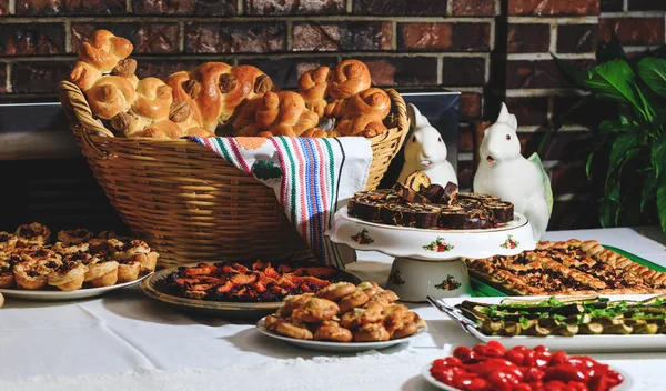 Tavolo pasquale con pane tradizionale e autentico cibo rumeno. Panini al forno, colaci o torte in cestini di paglia e asciugamano con motivi rustici. Pane sotto forma di lumache o piccioni nell'asciugamano colorato con elementi della cultura europea . — Foto Stock