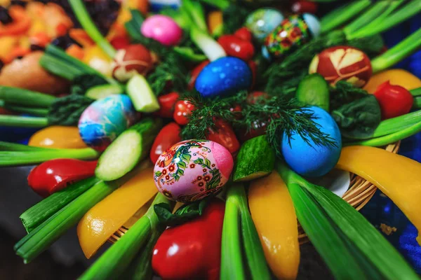 Paskalya süslenmiş yumurta ve sebzeler tatil masasında çiçek. Yumurtadan, baklagillerden, soğandan, biberden, domateslerden, salatalıktan oluşan yaratıcı bir besin bileşimi. Sanatsal renkli yemeklerin resmini kapat.