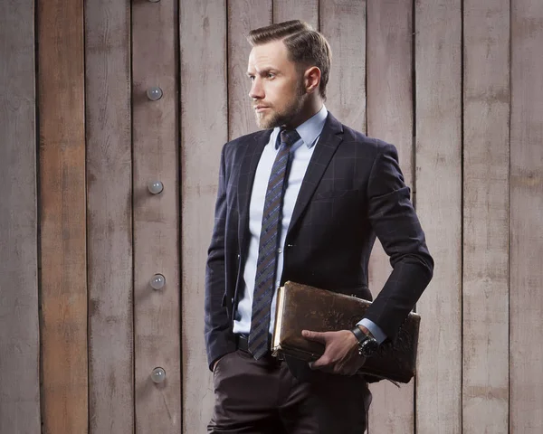 Portrait of brutal man in suit with old book in hand on wooden planks background