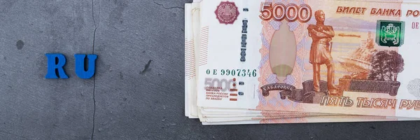 Big stack of Russian money banknotes of five thousand rubles lying on a grey cement background.