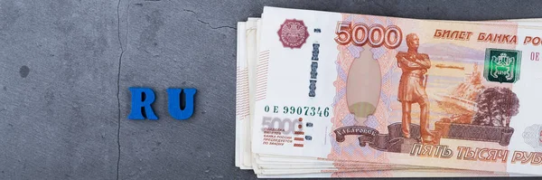 Big stack of Russian money banknotes of five thousand rubles lying on a grey cement background.