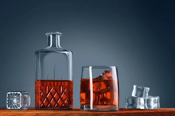 A glass of whiskey or cognac, a decanter and ice cubes, close-up on a wooden table. Blue background. Space for labels, text, and logo. Layout for advertising.