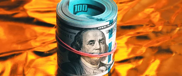 A roll of one hundred American dollars in close-up on a burning bright gold background. Close-up, full-contrast color image. Free space for labels and text.