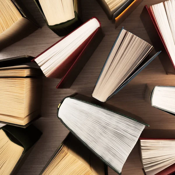 Books on the table, top view. In books, the sheets are spread out in the form of a fan, the shadows of books on a light wooden table. Back to school. Training, education, reading, science.