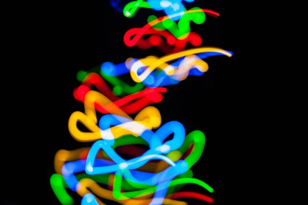 Colorful bright red, yellow, blue and green mixed Christmas lights flowing in various directions creating abstract movement on a black background