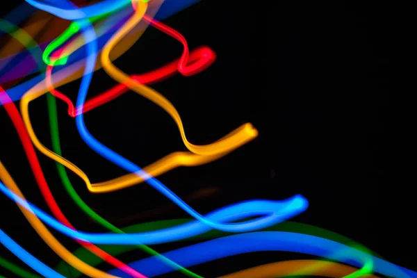 Colorful bright red, yellow, blue and green mixed Christmas lights flowing in various directions creating abstract movement on a black background