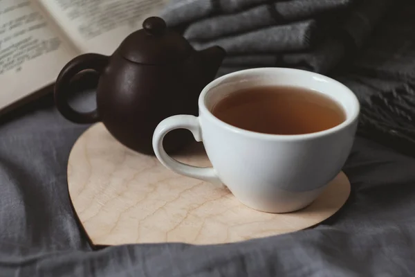 Чашка чая и чайник на деревянной книге сердца и шарф — стоковое фото