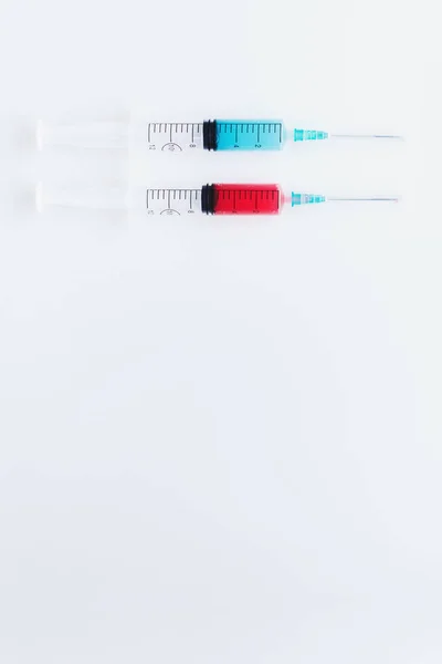 Два шприци, наповнені синьо-червоними рідинами на білому фоні — стокове фото