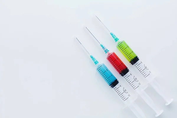 Three syringes filled with blue, red and green liquids on white — 图库照片