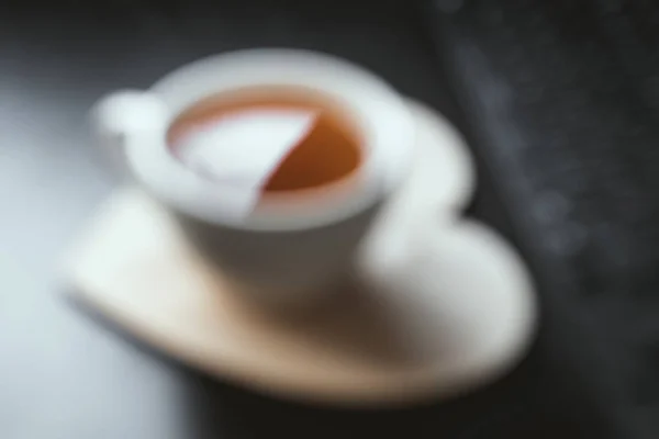 Taza de té blanco borrosa en placa de madera en forma de corazón — Foto de Stock