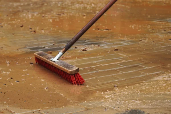 Kırmızı plastik, pürüzlü fırça, kumu temizliyor ve su, taş kaldırımı kaplıyor.