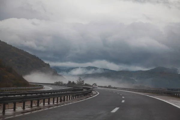구름낀 안개낀 산들이 내려다 보이는 왼쪽으로 회색의 아스팔트 — 스톡 사진