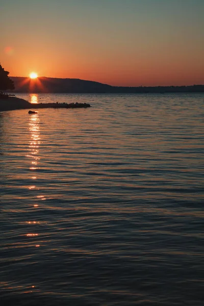 水の上に昇る太陽と反対側の海岸の遠くの丘のミニマルな写真 — ストック写真