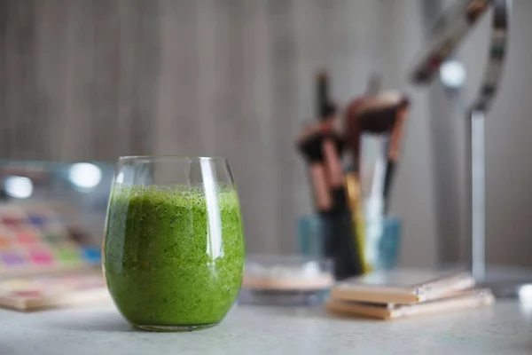Makyaj masasında yeşil smoothie ile dolu şeffaf cam. Güzel ve sağlıklı olma kavramı hem içeride hem de dışarıda..