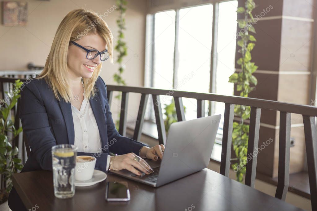 Business woman is working on computer and drinking cup of coffee and glass of water in a coffee shop, restaurant