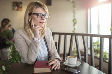 Bir restoranda bir kitap okuma ve kahve içme sarışın genç gülümseyen kadın