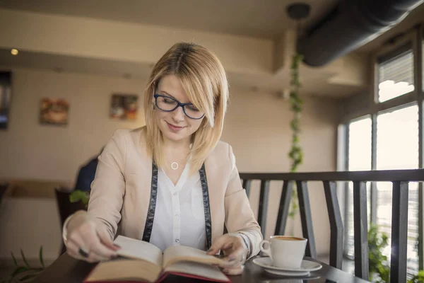 Bir restoranda bir kitap okuma ve kahve içme sarışın genç gülümseyen kadın