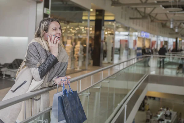 Mosolygó lány beszél vele mobiltelefon bevásárlóközpontban, miközben — Stock Fotó