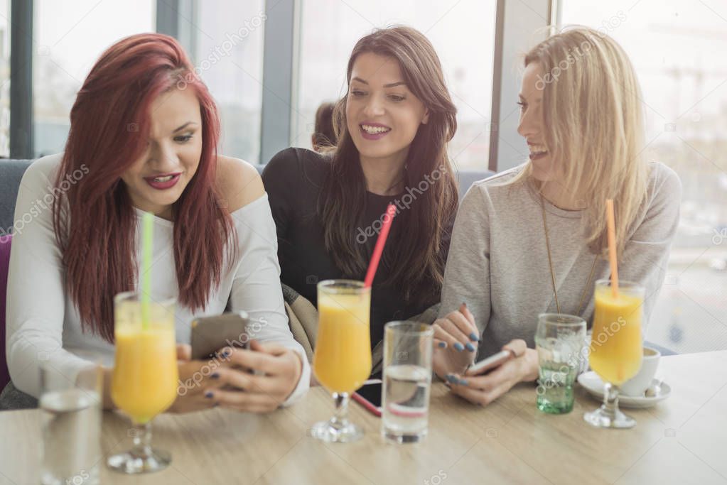 Portrait of three young beautiful women using mobile phone at co