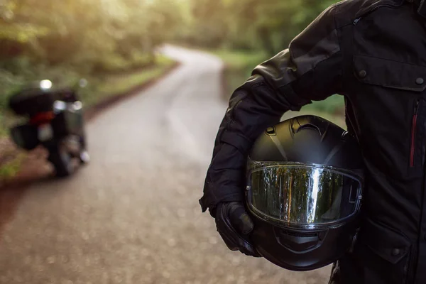 Raiders kıyafetli motosikletli adam, hazırlanıyor. Gün batımında genç bir adam motosikletin yanında duruyor. Yolda motosikletli bir motorsikletli. Motosiklet ve güvenli sürüş. Kask ve motosiklet.
