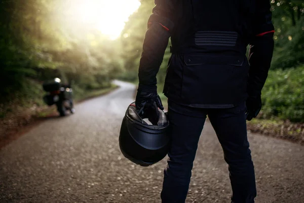 Raiders kıyafetli motosikletli adam, hazırlanıyor. Gün batımında genç bir adam motosikletin yanında duruyor. Yolda motosikletli bir motorsikletli. Motosiklet ve güvenli sürüş. Kask ve motosiklet.