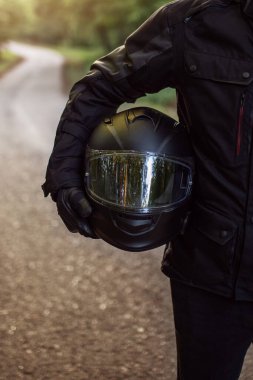 Raiders kıyafetli motosikletli adam, hazırlanıyor. Gün batımında genç bir adam motosikletin yanında duruyor. Yolda motosikletli bir motorsikletli. Motosiklet ve güvenli sürüş. Kask ve motosiklet.