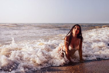 Beyaz mayo giymiş bir kız kumlu sahilde uzanıyor ve çok güzel bir köpük dalgasını örtüyor. Dinlenme konsepti, yaşam tarzı ve iyi ruh hali.
