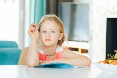 Masadaki küçük kız elinde defter, ödev yapıyor..