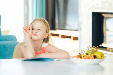 Masadaki küçük kız elinde defter, ödev yapıyor..