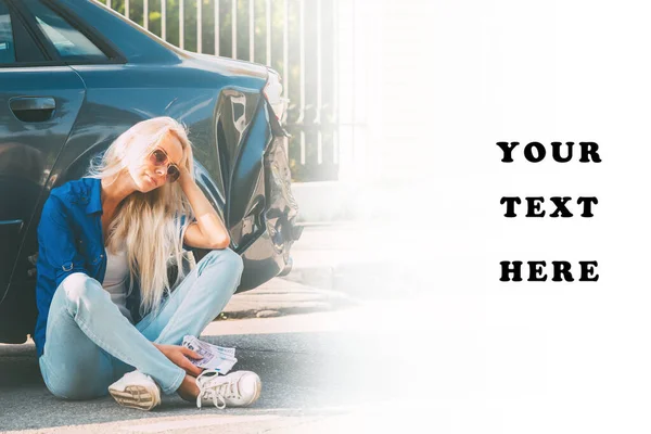 The girl sits at the broken car with money bills for repair.