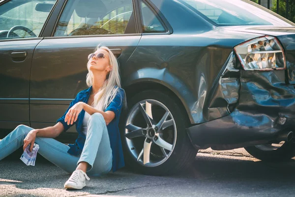 The girl sits at the broken car with money bills for repair.